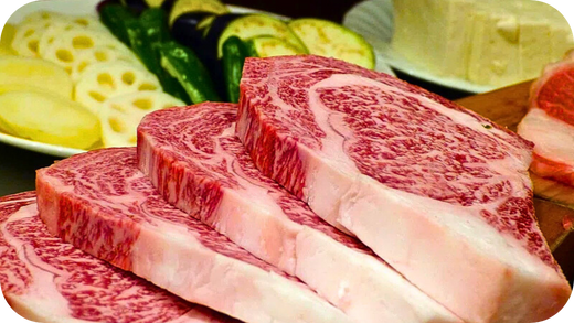 Several thick-cut, highly marbled Wagyu ribeye steaks fanned out next to plates of sliced vegetables ready for grilling.