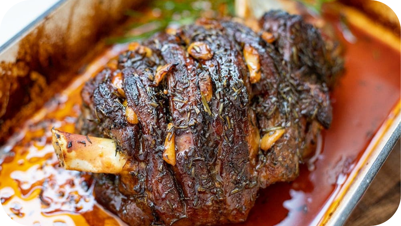 Slow-cooked lamb roast in a baking tray, seasoned with herbs and garlic in rich juices.