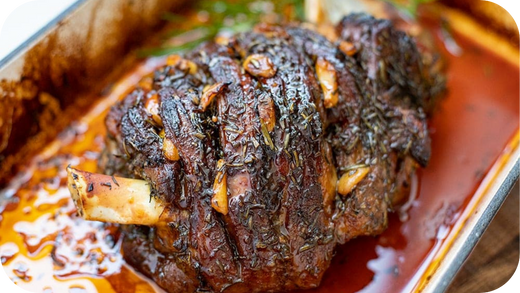 Slow-cooked lamb roast in a baking tray, seasoned with herbs and garlic in rich juices.