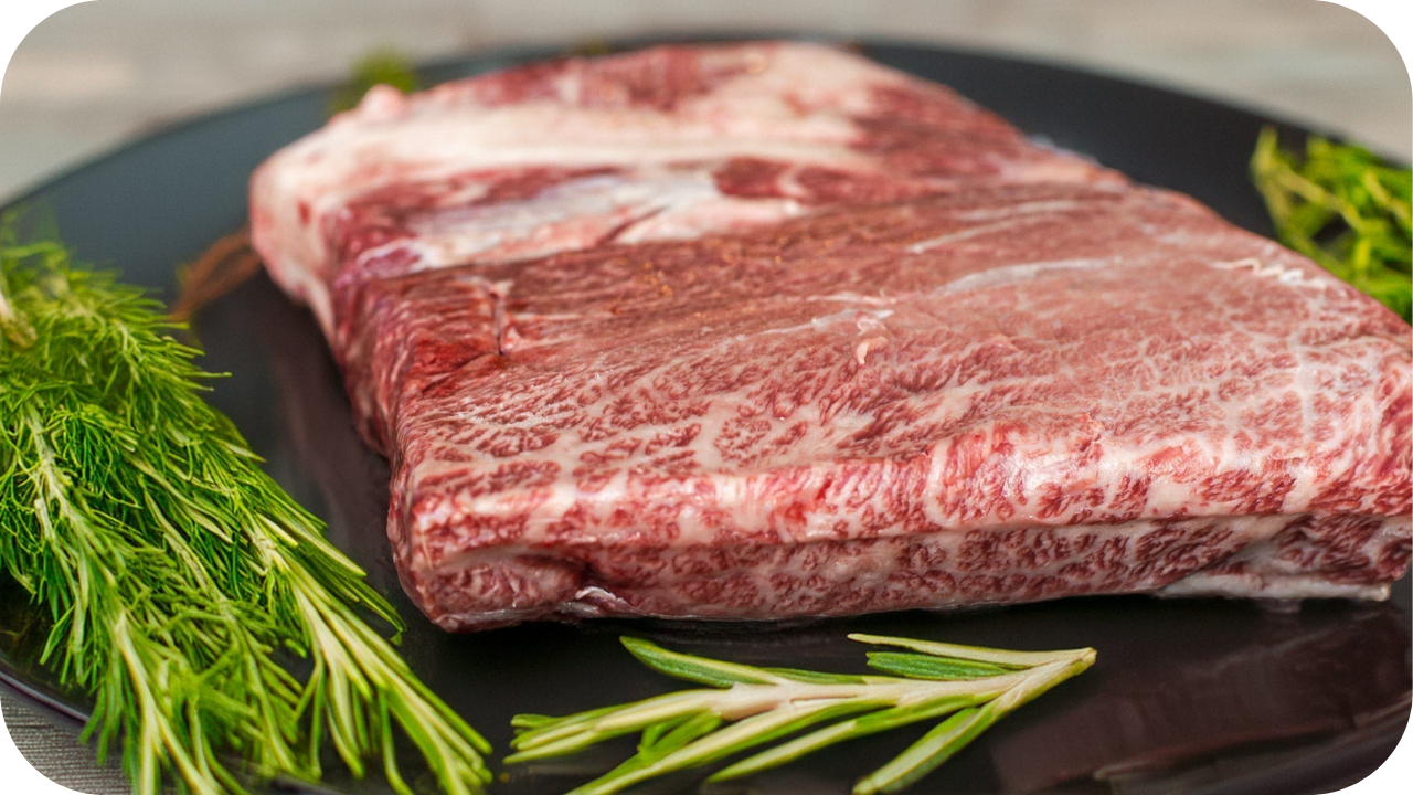Raw Wagyu steak with visible marbling on a black plate surrounded by fresh rosemary, ready for cooking in a step-by-step Wagyu guide.