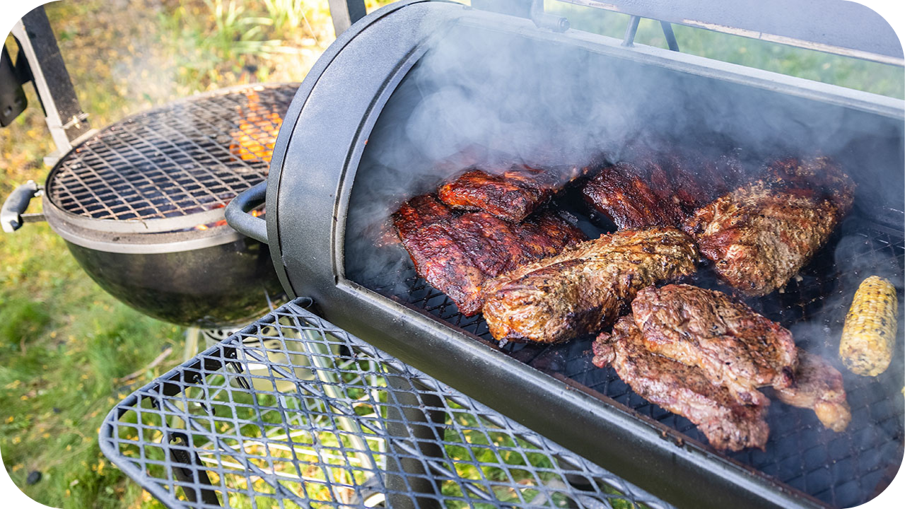 Assorted steak cuts grilling over charcoal in a backyard BBQ smoker, surrounded by smoke and corn, showing different textures and sear levels.