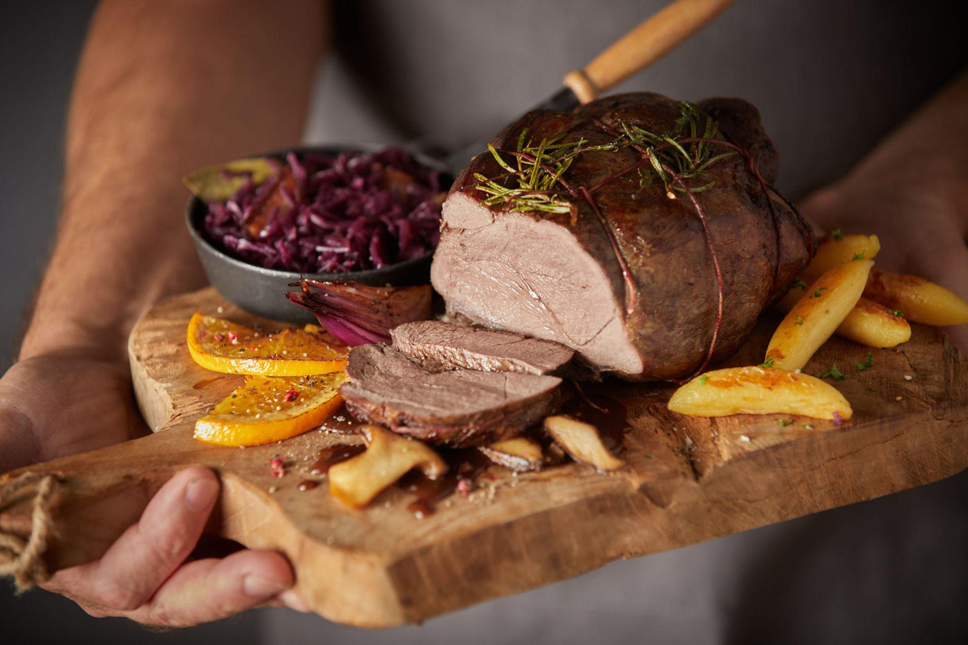 Medium-rare beef eye fillet roast sliced on a wooden board, garnished with rosemary, served with roasted potatoes, sauteed mushrooms and red cabbage
