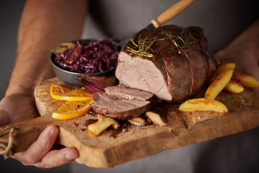 Medium-rare beef eye fillet roast sliced on a wooden board, garnished with rosemary, served with roasted potatoes, sauteed mushrooms and red cabbage