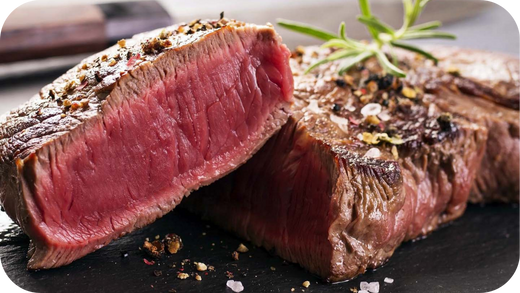 Premium steak sliced to reveal a rare centre, garnished with herbs, salt, and cracked pepper on a dark board.