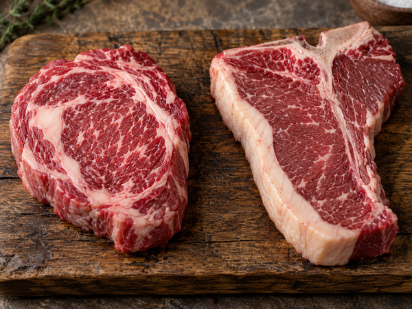 Raw scotch fillet and porterhouse steak side by side showing marbling and fat cap differences