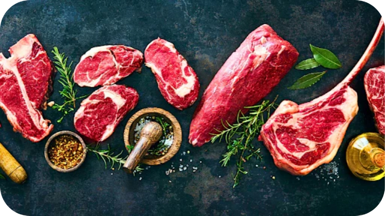 Fresh raw beef cuts, including rib eye, sirloin, and tomahawk steak, arranged on a dark board with herbs, spices, and oil for a low-carb cooking preparation scene.