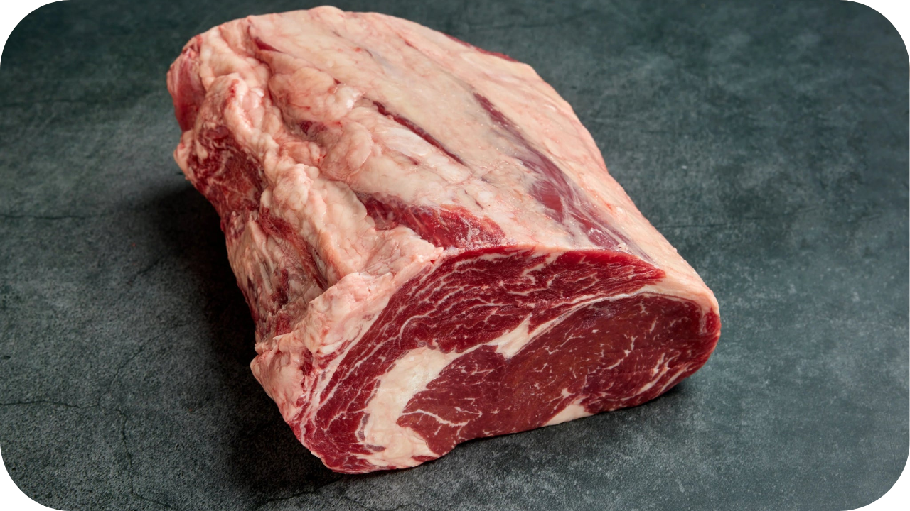A single raw Bass Strait Cube Roll cut resting on a dark stone surface, showing deep red meat with intricate white marbling and a thick fat cap.