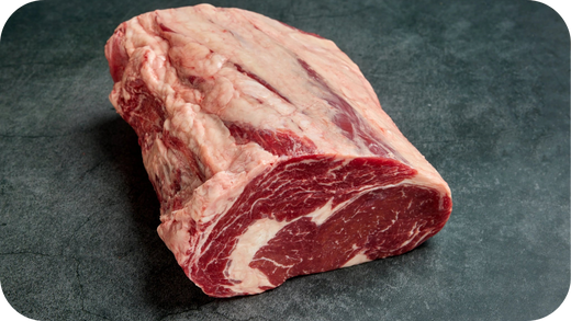 A single raw Bass Strait Cube Roll cut resting on a dark stone surface, showing deep red meat with intricate white marbling and a thick fat cap.