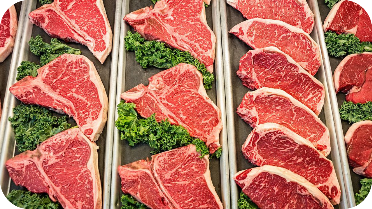 Fresh beef steaks displayed in butcher trays with greens, highlighting marbling and healthy fats in grass fed meat cuts.