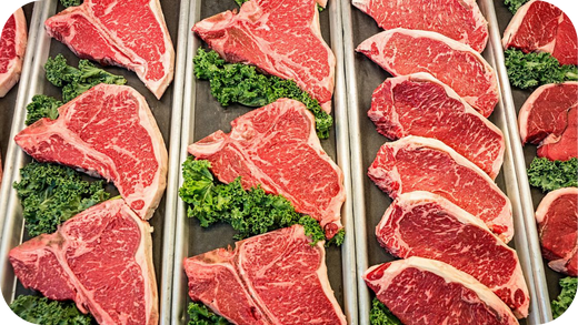 Fresh beef steaks displayed in butcher trays with greens, highlighting marbling and healthy fats in grass fed meat cuts.