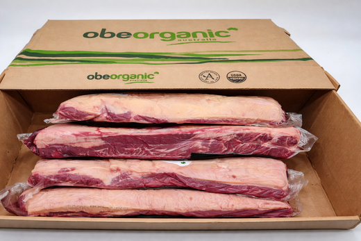  Open OBE Organic Australia cardboard box with four vacuum sealed beef striploin cuts stacked inside, organic certified packaging visible.