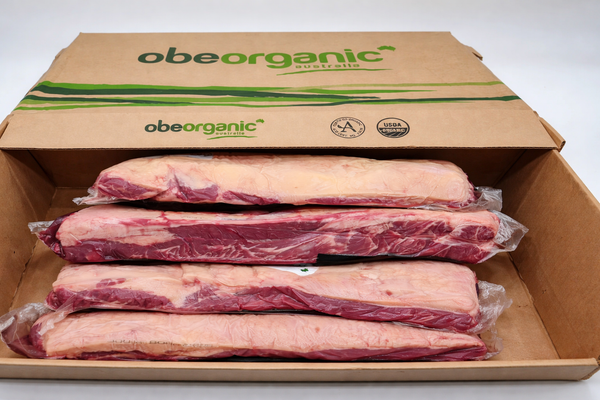  Open OBE Organic Australia cardboard box with four vacuum sealed beef striploin cuts stacked inside, organic certified packaging visible.
