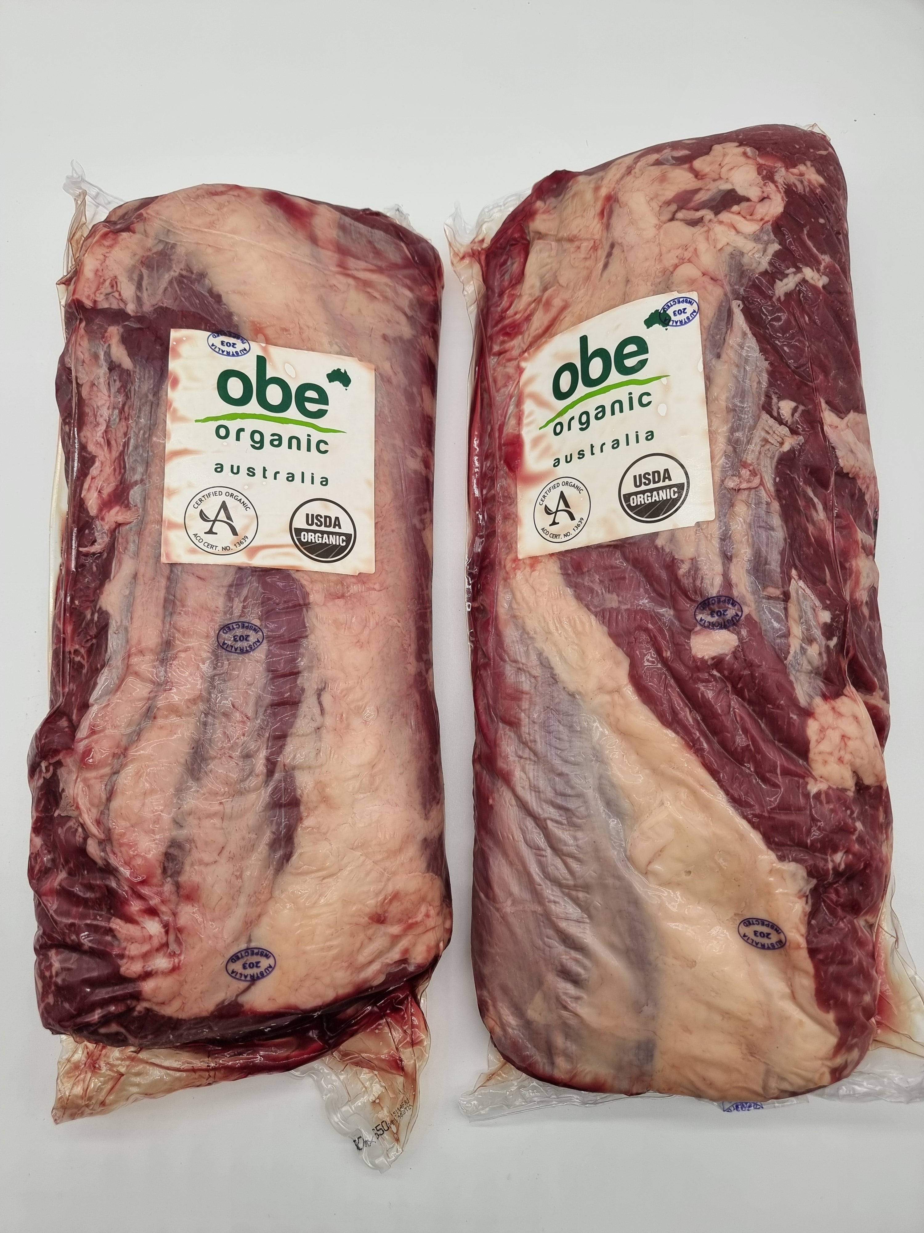 Two packages of raw meat with 'obe organic' labels on a white background